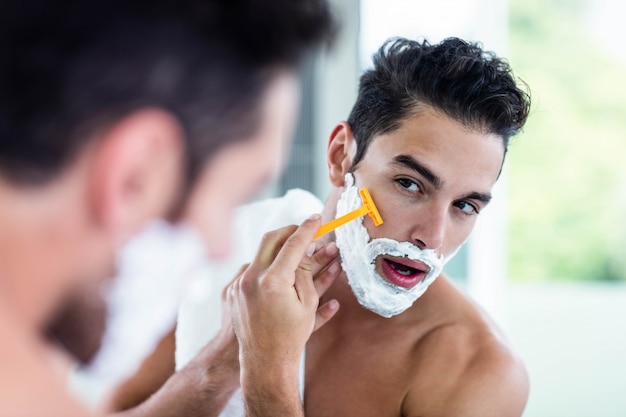 Hombre guapo afeitándose la barba en el baño