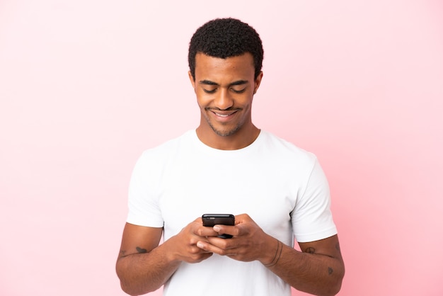 Hombre guapo afroamericano sobre fondo rosa aislado enviando un mensaje o correo electrónico con el móvil