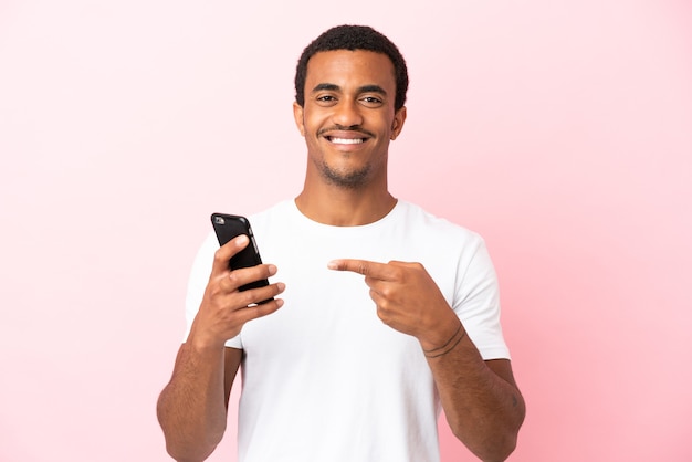 Hombre guapo afroamericano sobre fondo rosa aislado con teléfono móvil y apuntando