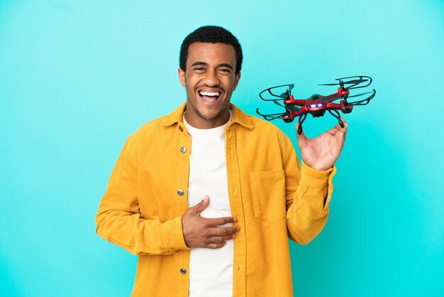 Hombre guapo afroamericano sosteniendo un avión no tripulado sobre fondo azul aislado sonriendo mucho