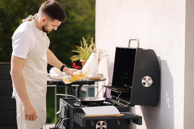 Hombre guapo agregue aceite en la sartén preparando comida concepto de barbacoa al aire libre en la terraza