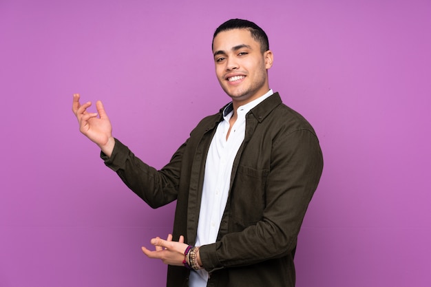 Hombre guapo aislado en la pared azul extendiendo las manos a un lado para invitar a venir