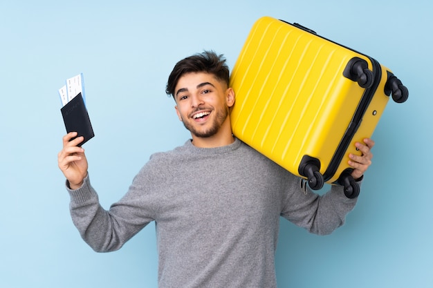 Hombre guapo aislado en la pared azul en vacaciones con maleta y pasaporte