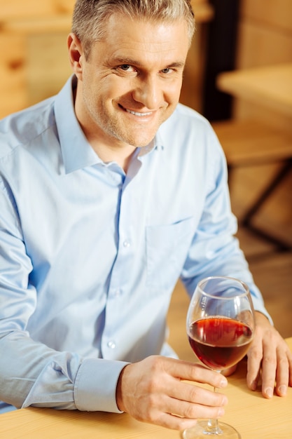 Foto hombre guapo alegre bien construido sonriendo y sosteniendo una copa de vino mientras disfruta de su fin de semana