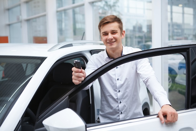 Hombre guapo alegre mostrando la llave del coche, celebrando la compra de un auto nuevo en el concesionario