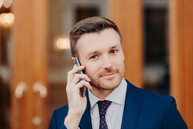 Hombre guapo con apariencia atractiva, habla por teléfono celular