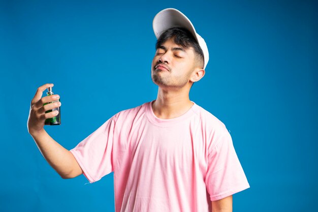 Hombre guapo aplicando perfume a distancia sobre un fondo azul