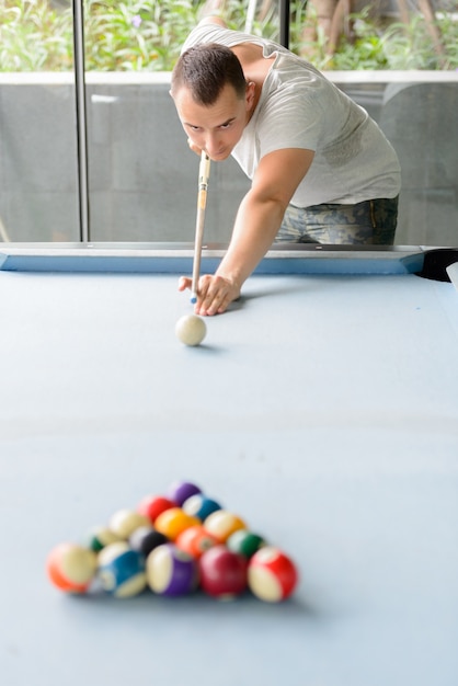 Foto hombre guapo apoyado en la mesa de billar mientras juega al billar