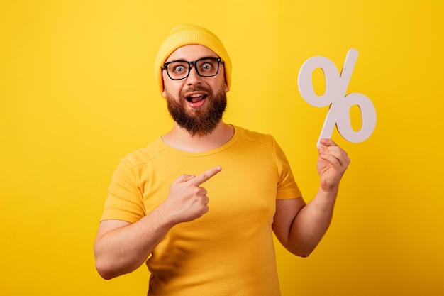 Hombre guapo apuntando al símbolo de porcentaje sobre fondo amarillo, concepto de préstamo sin intereses