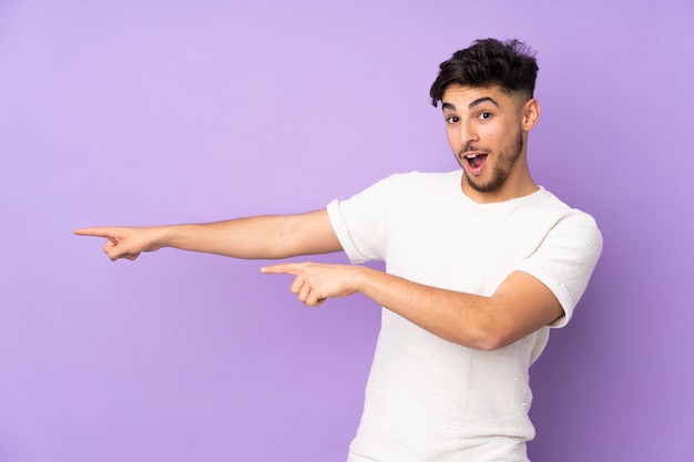 Hombre guapo árabe sobre pared apuntando con el dedo al lado