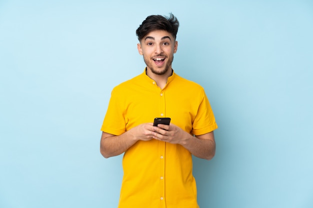 Hombre guapo árabe sobre pared sorprendido y enviando un mensaje