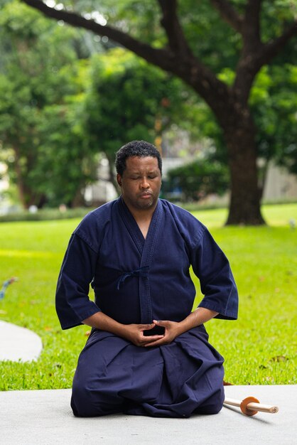 Hombre guapo artista marcial negro con traje de artes marciales de kendo haciendo meditación