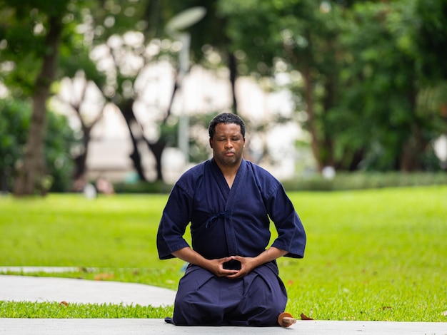 Foto hombre guapo artista marcial negro con traje de artes marciales de kendo haciendo meditación