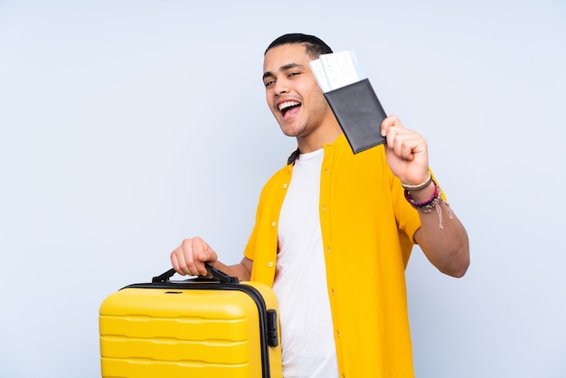 Hombre guapo asiático aislado sobre fondo azul en vacaciones con maleta y pasaporte