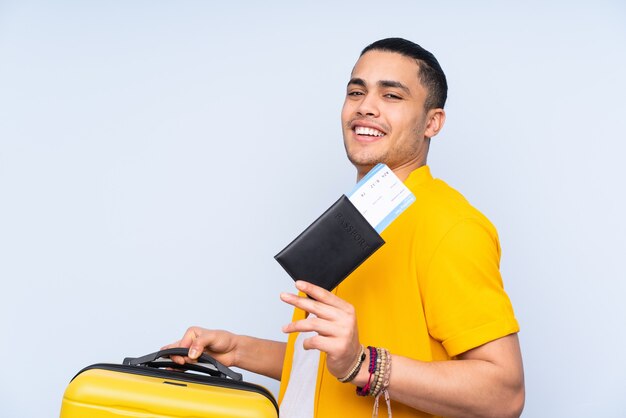 Hombre guapo asiático aislado sobre fondo azul en vacaciones con maleta y pasaporte