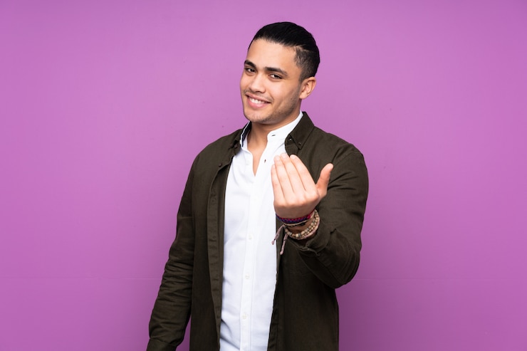 Foto hombre guapo asiático en pared azul invitando a venir con la mano.