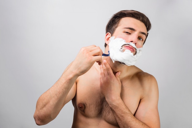 El hombre guapo y atractivo está en el proceso de afeitarse la barba. No se arrepiente de eso. Este hombre usa muy buena cuchilla. Concepto de publicidad. Vista de corte