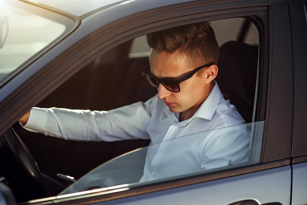 Hombre guapo atractivo en gafas de sol con teléfono inteligente en su coche