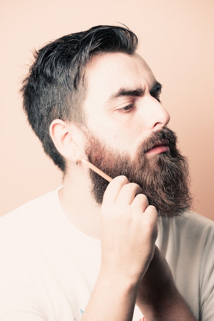 Hombre guapo con barba afeitándose la barba, joven barbudo caucásico recortando la barba en casa durante la cuarentena. Concepto de estilo de vida.