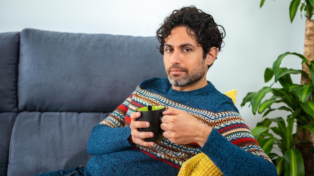 Hombre guapo con barba bebiendo café expresso matutino con cara feliz sonriendo y mirando a la cámara en el sofá de casa. Persona positiva.