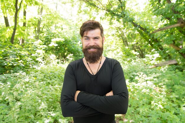 Hombre guapo con barba y bigote vacaciones de verano Brutalidad del concepto de selvas Concepto de temporada de calor de verano Naturaleza salvaje Hombre barbudo hipster fondo de follaje brillante Chico relajarse en el bosque de verano