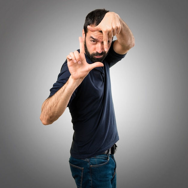 Foto hombre guapo con la barba centrándose con sus dedos sobre fondo gris