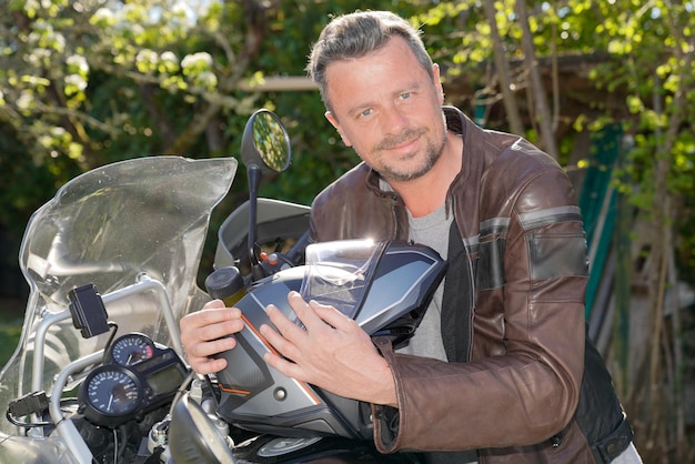 hombre guapo con barba en chaqueta de moto marrón casco de motocicleta en las manos