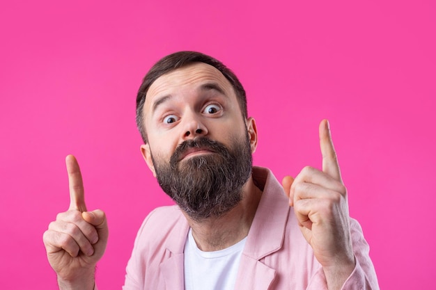 Un hombre guapo con barba en una chaqueta rosa está pensando en un fondo rojo aislado