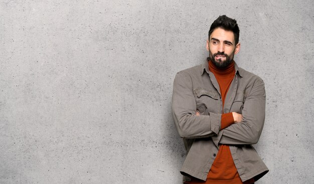 El hombre guapo con barba confunde la expresión de la cara mientras muerde el labio sobre la pared con textura