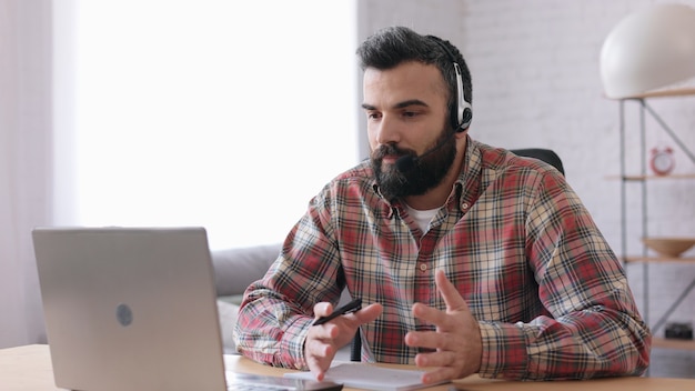 Hombre guapo con barba enseñando en línea hablando con la cámara web de la computadora portátil. Educación en línea, trabajo a distancia.