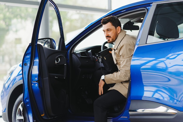 Hombre guapo con barba está acariciando su nuevo coche y sonriendo