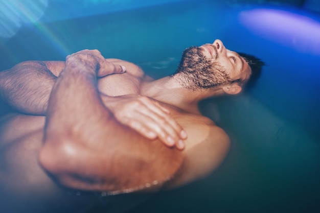 Hombre guapo con barba flotando en un tanque lleno de agua salada densa utilizada en meditación, terapia y medicina alternativa.