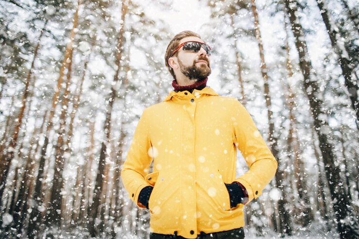 Hombre guapo con barba en gafas de sol espejadas posando en el bosque de invierno
