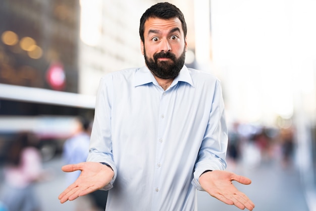 Hombre guapo con barba haciendo gesto sin importancia sobre fondo desenfocado