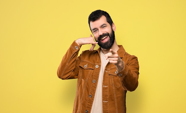 Hombre guapo con barba haciendo gesto de teléfono y apuntando frente