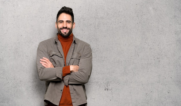 Hombre guapo con barba manteniendo los brazos cruzados en posición frontal sobre la pared con textura