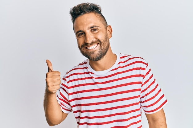 Hombre guapo con barba con ropa informal sonriendo feliz y positivo pulgar hacia arriba haciendo excelente y signo de aprobación