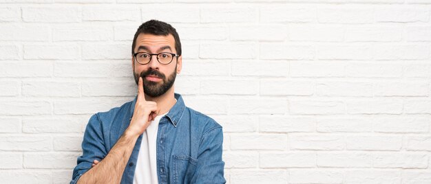 Foto hombre guapo con barba sobre pared de ladrillo blanco mirando al frente