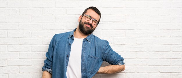 Hombre guapo con barba sobre pared de ladrillo blanco que sufre de dolor de espalda por haber hecho un esfuerzo