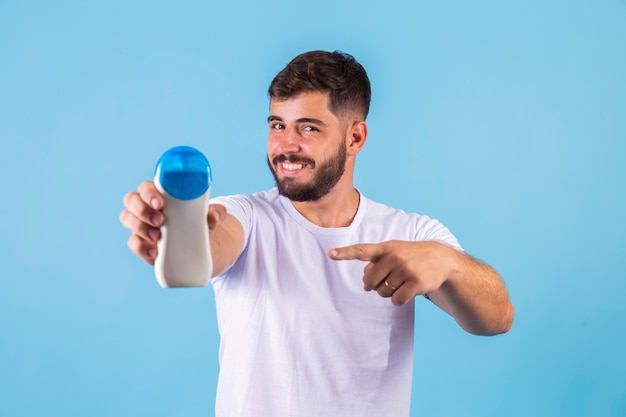 Hombre guapo con barba de vacaciones usando traje de baño sosteniendo una botella de loción de protección solar luciendo positivo y feliz de pie y sonriendo con una sonrisa segura mostrando los dientes