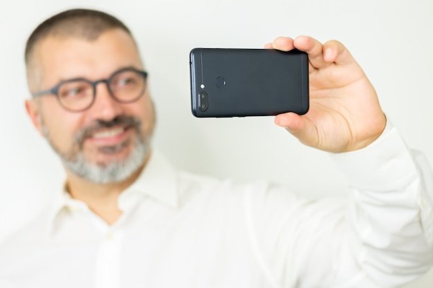 Hombre guapo con barba vestido con camisa y gafas tomando selfie o se comunica en línea