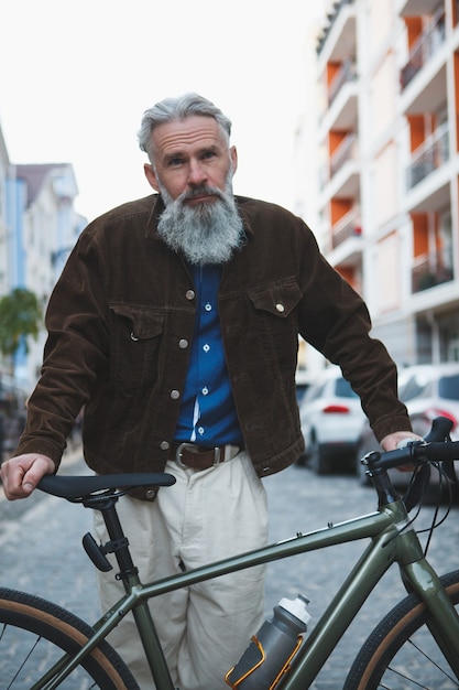 Hombre guapo con barba vistiendo ropa de calle elegante de pie con su bicicleta