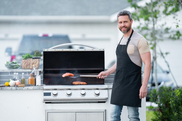 Hombre guapo barbacoa en una parrilla en el patio trasero cocinar al aire libre y concepto de estilo de vida estadounidense