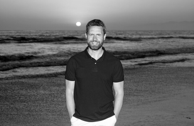 Hombre guapo barbudo feliz en camisa de verano en la playa con puesta de sol sobre el verano del mar