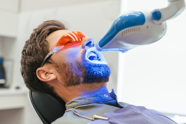 Hombre guapo barbudo paciente blanqueo de dientes en la clínica dental moderna tratamiento de dientes concepto de atención médica