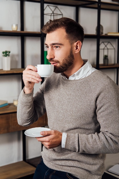 Hombre guapo bebiendo café y mirando a casa