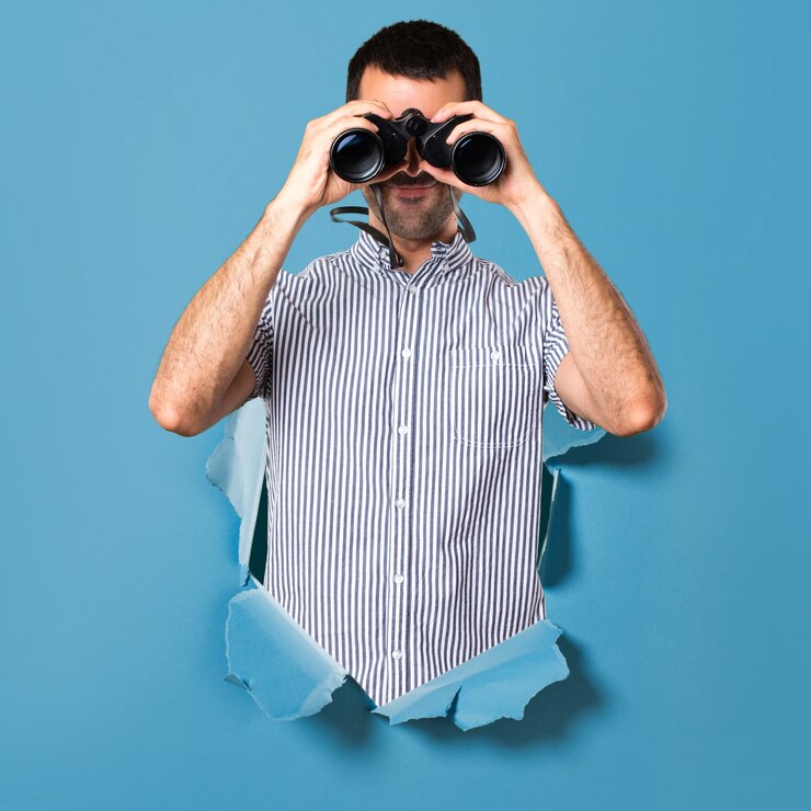 Foto hombre guapo con binoculares a través de un agujero de papel