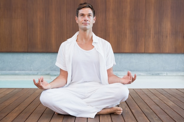 Hombre guapo en blanco meditando en postura de loto