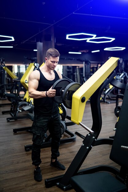 Hombre guapo con buen entrenamiento de bíceps. Joven musculoso entrenando duro en el gimnasio.