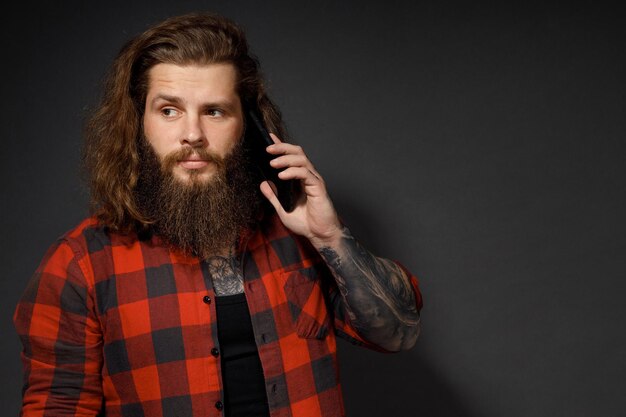 Hombre guapo con cabello largo sosteniendo un teléfono móvil junto a la oreja.